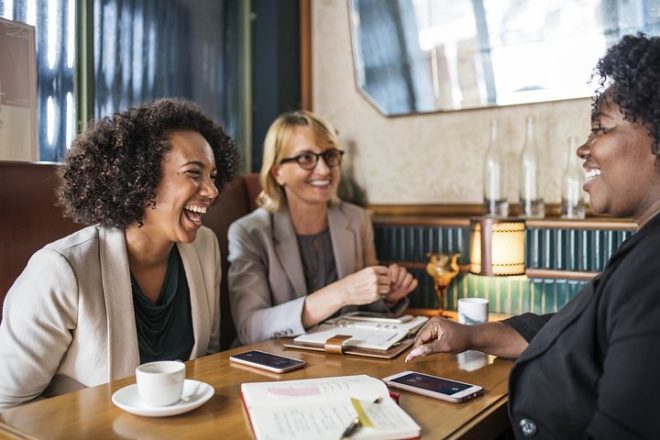 Three women laughing and chatting at a café.